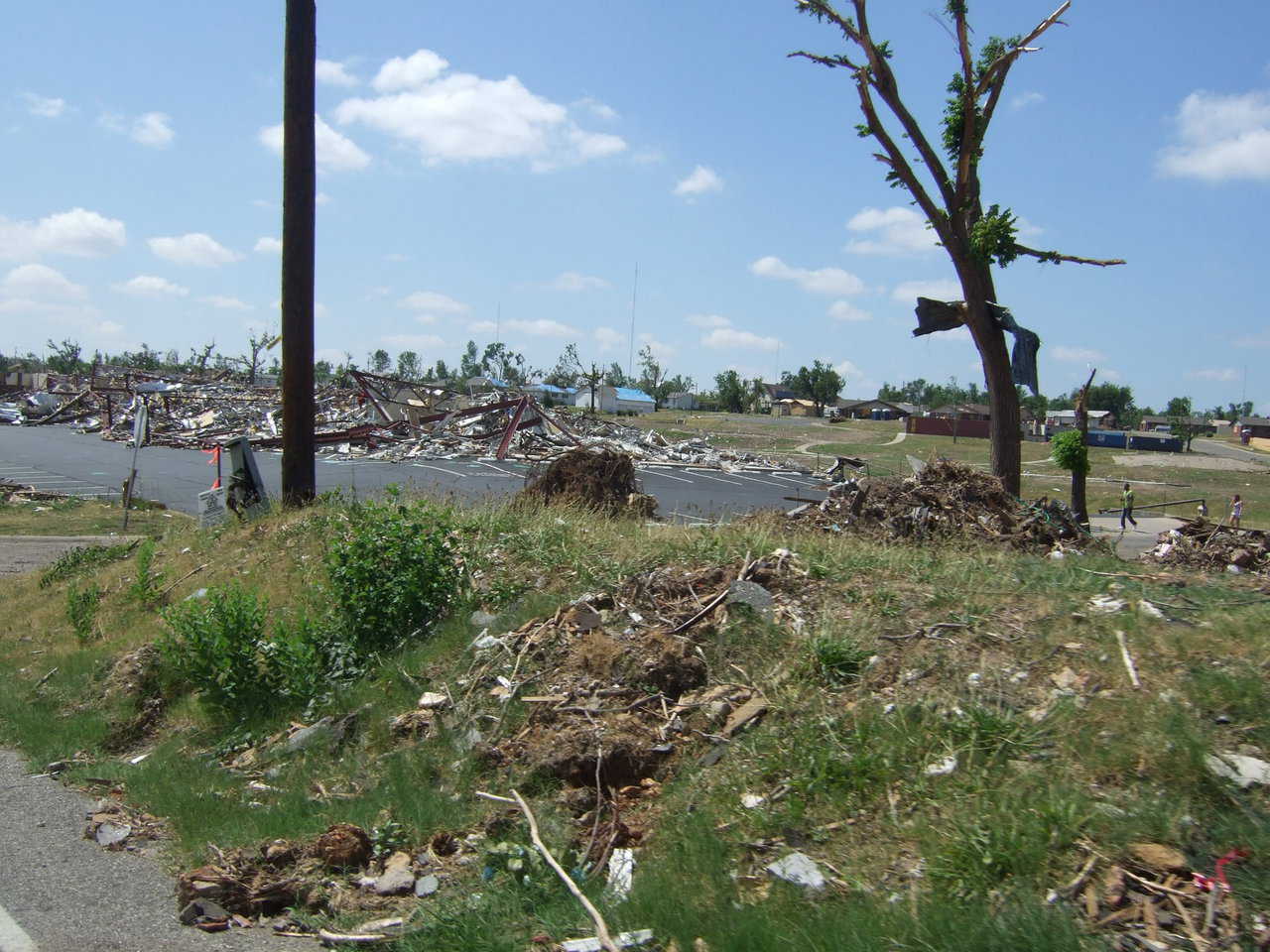 Houses in the background are covered with blue tarps. Although not destroyed, they received severe damage.