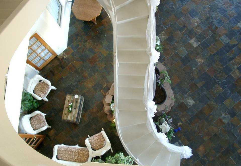 View from the third floor — Stone tile flooring provides an earthy-feel and generates a striking contrast to the white staircase and wicker furniture.