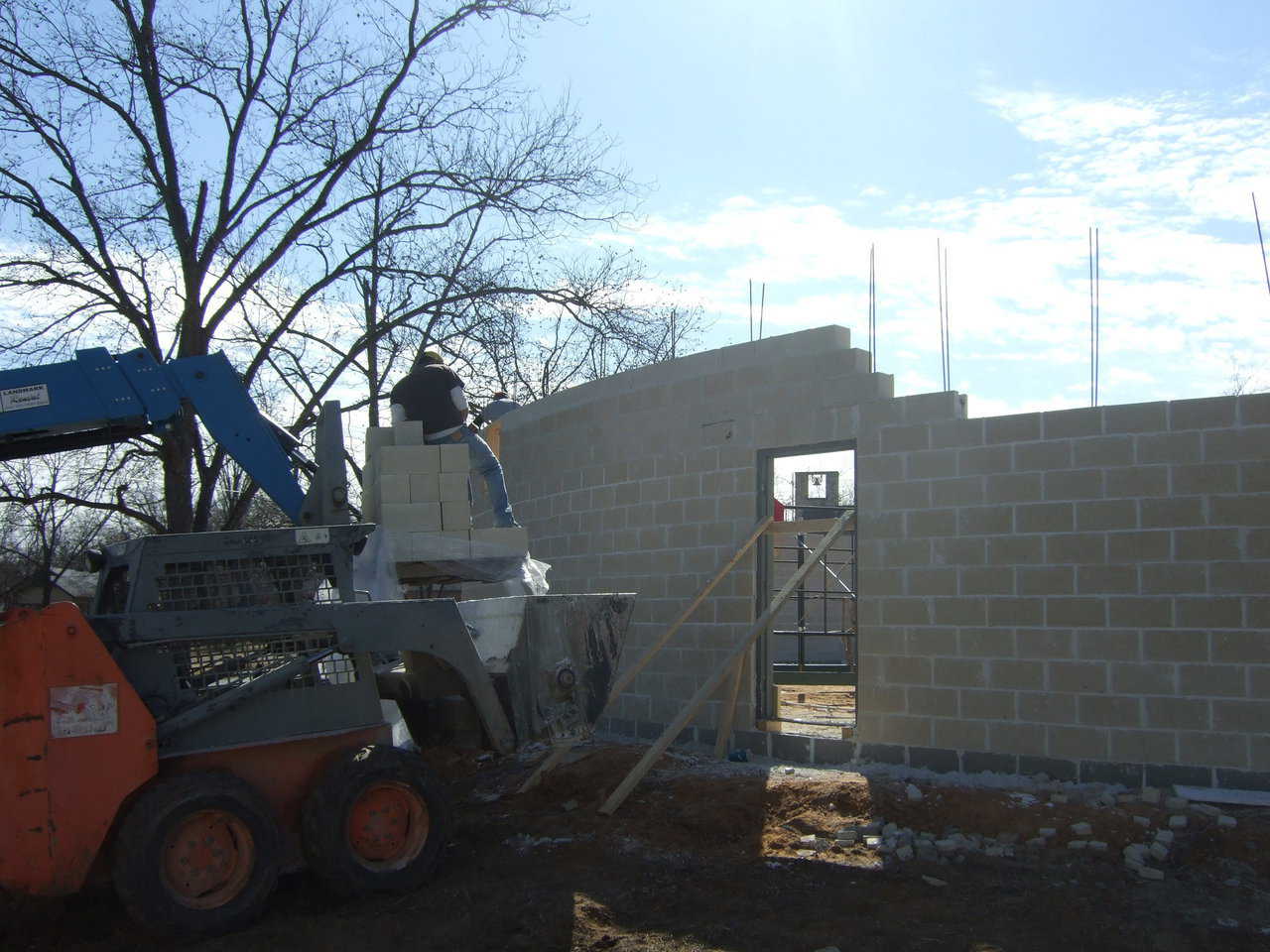 Image form the outside. The forklift is delivering the blocks, and the skid steer is delivering the mud. The bobcats ability to go through even the roughest territory makes moving the mortar very simple. Imagine using wheel barrow through that mud, or even moving the mud in a standard skid steer bucket without loosing half the batch.