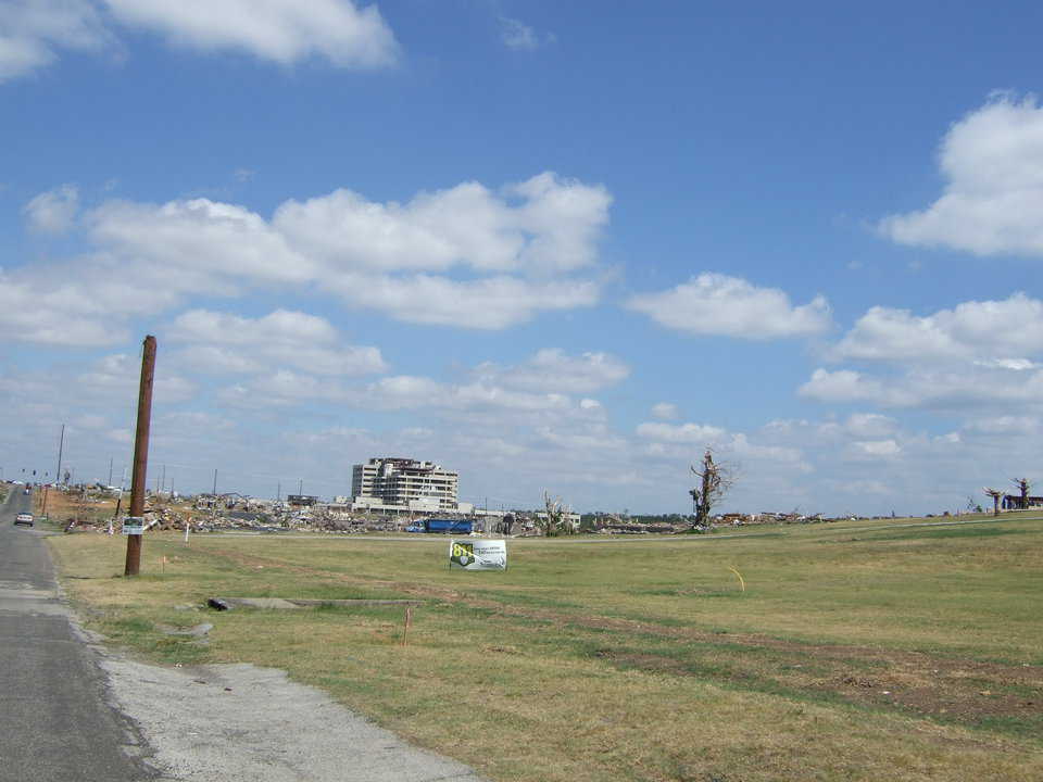 A beyond-salvage hospital is in the background and the area all around it is flattened.