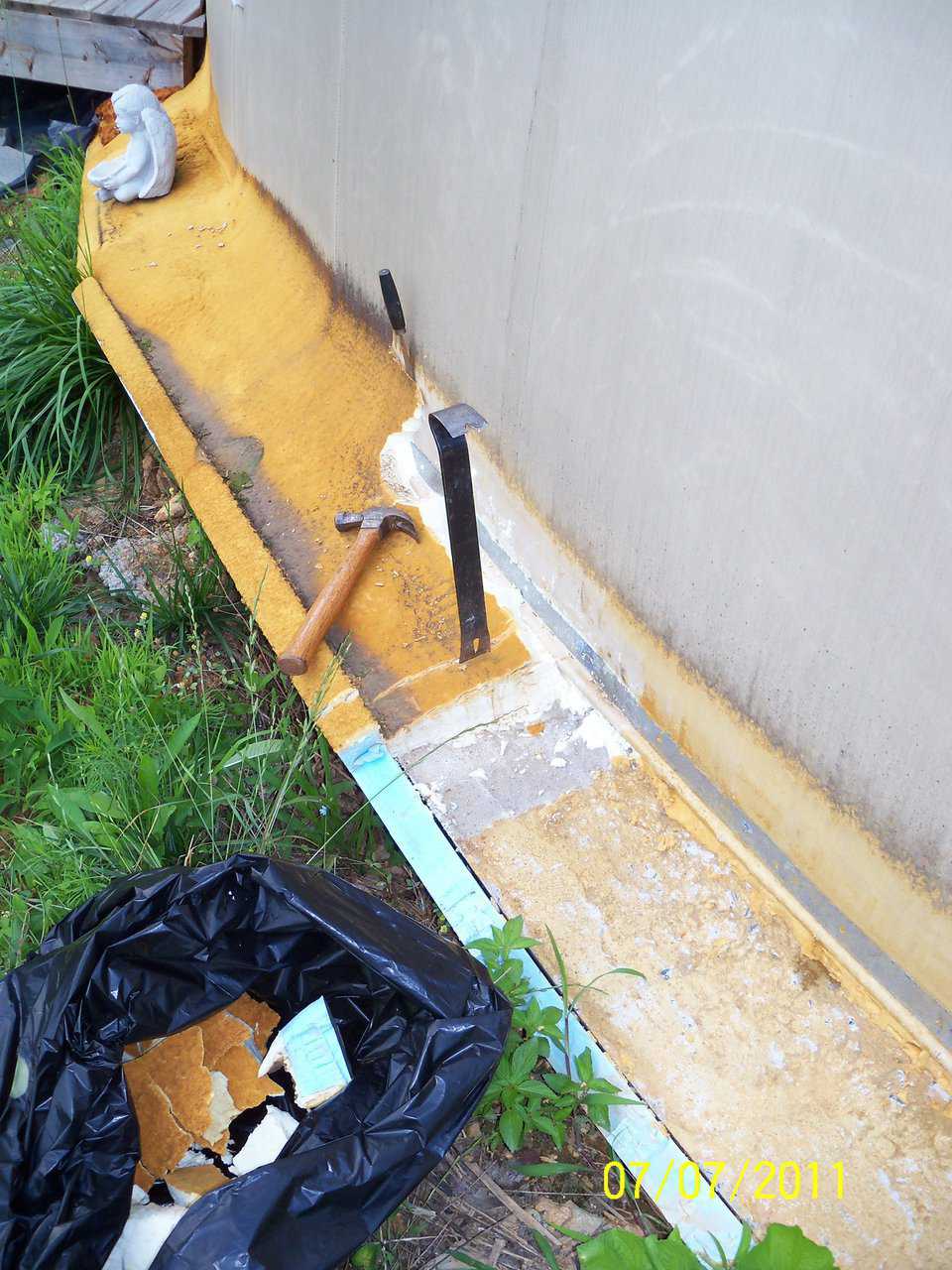 Off with the band! — two years later the foam band was chiseled off the foundation so exterior finish work could begin. In the photo’s lower right corner, note the tanned UV discoloration on the foam’s surface and the small puddle along the metal strapping.