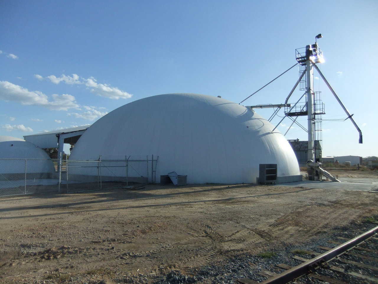A view of the back — Shown here is the completed facility from the rear. You can see the unloading can be done from the rail or trucks. Product can go back into trucks or into the building. To the left you can see the small dome and the canopy over the mixing facility.