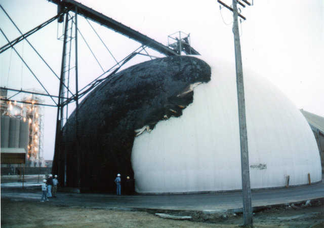 Fire damage from three wood structures and 300 gallons of transformer oil – Cargill – Channelview, TX
A violent, wind-driven fire fueled by three wood structures and 300 gallons of transformer oil burned about a third of the covering off this fertilizer storage. The fire was the worst possible. Late at night, wind blew the fire directly toward the building. The fire department was not immediately called, so the oil burned completely. Damage was most severe to the exterior. In a 12-square-foot area, urethane was totally burned off, but the rest suffered more minor damage. The foam could be cleaned and a coating or metal cladding could be installed over it. No damage was detected on the inside of the Monolithic Dome.
Note that the foam held the fire back for a considerable time, and then the nonflammable concrete ended any possibility of the flames burning through to the stored product. Materials inside the dome were totally unaffected by the fire, and the dome’s concrete interior never even got warm.