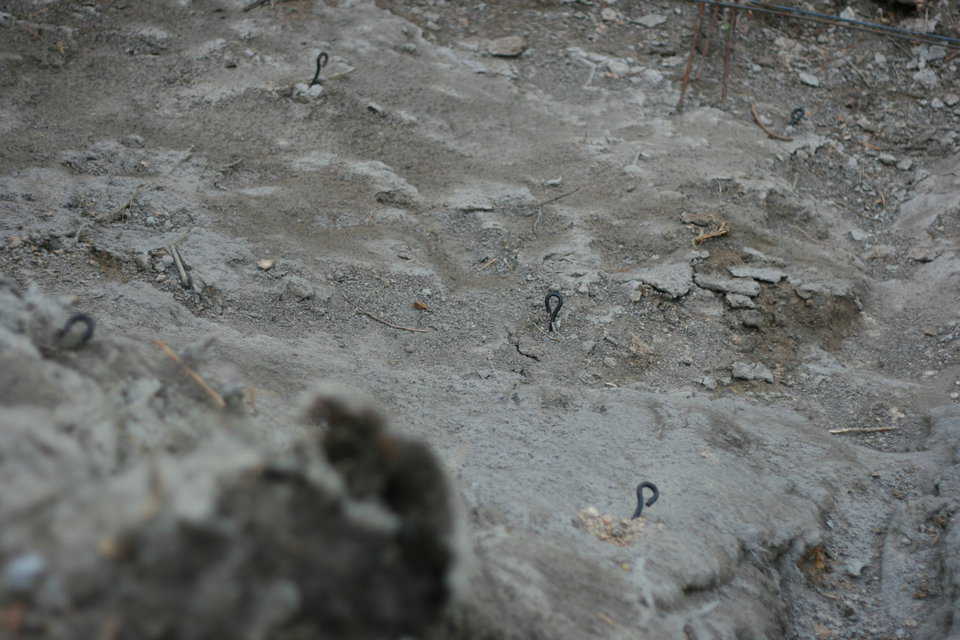 Notice the round rings sticking out of the earth. Those are attached to ground anchors we call mobile home anchors. At their far ends, they have a screw; they vary between two, four and five feet in length and are screwed into the earth.
