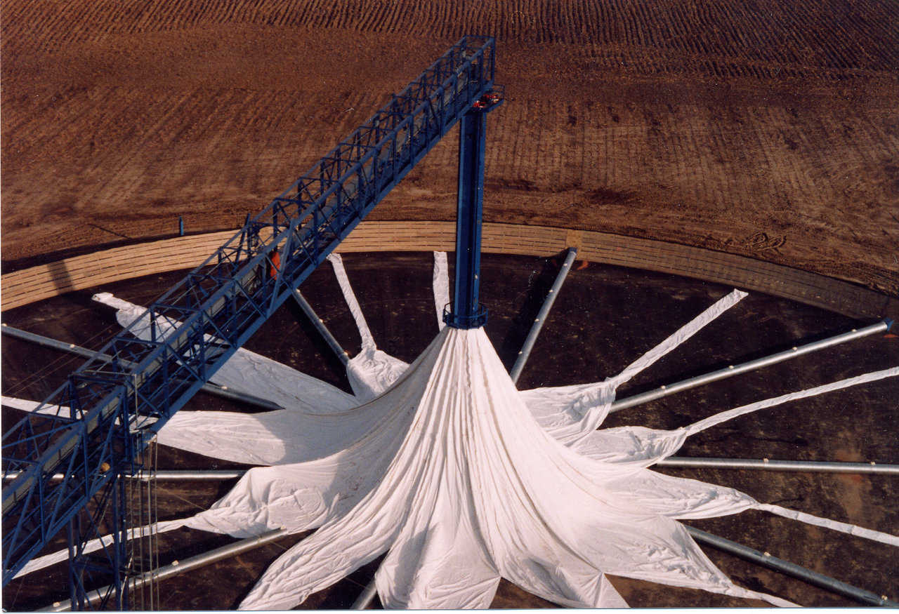 A tubelike tower, with a lifting ring that can slide up and down the tower, stands in the center of the grain cover. The middle of the grain cover fits around the tower, while its bottom is secured to the fence.
