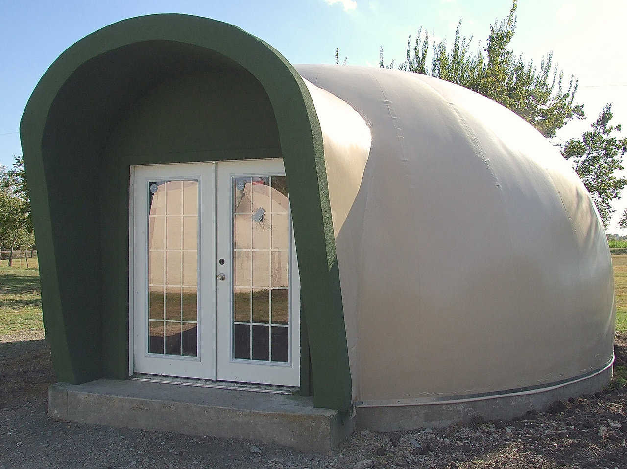 When Mike South built a new, small dome behind his home, he designed and built a tilted-out augment over the front entrance and the windows in back.  The front augment protects the door and provides shelter for folks entering the dome, while the back augment protects the windows.