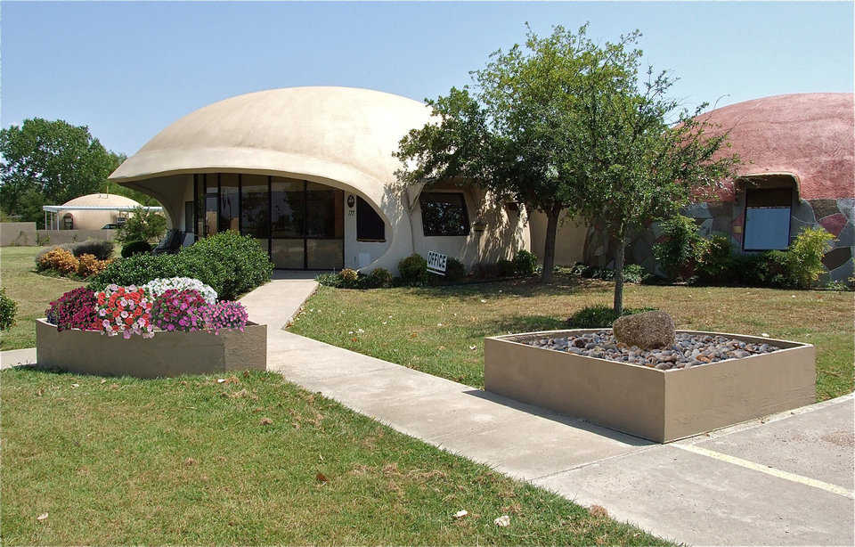 A pair of concrete planters enhance the entrance to the main offices of Monolithic Constructors, Inc. in Italy, Texas. The left planter contains a variety of flowers while the planter on the right is a rock garden featuring one stone which is the meaning of the word monolithic.