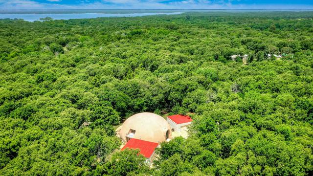 Aerial view of dome home among the forest trees and Lake Texoma in the background.